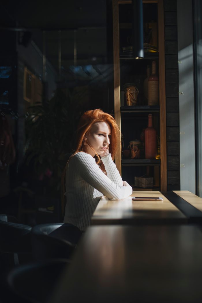 lone-young-woman-sitting-near-window-with-mobile-phone-table.jpg