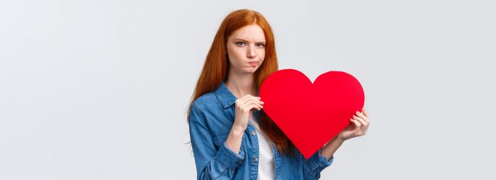 Serious-looking troubled, unsure cute redhead girl thinking what gift buy in addition to valentines day big red heart card, plan romantic date, pouting and frowning camera perplexed
