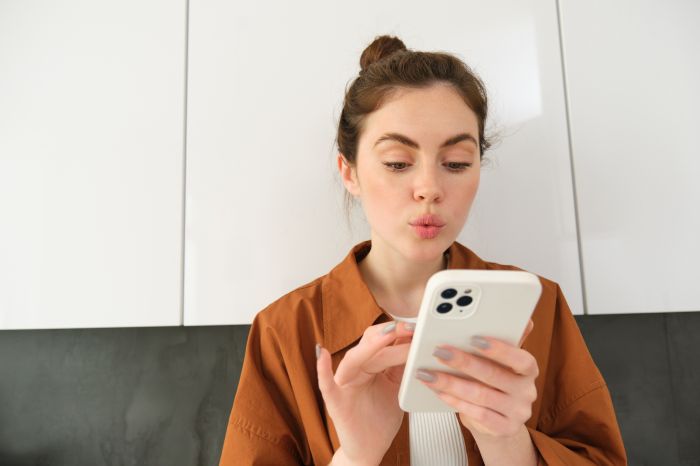Portrait of young woman at home, looking with interest at smartphone screen, concept of online shopping, buying on mobile apps, picking something using application on phone