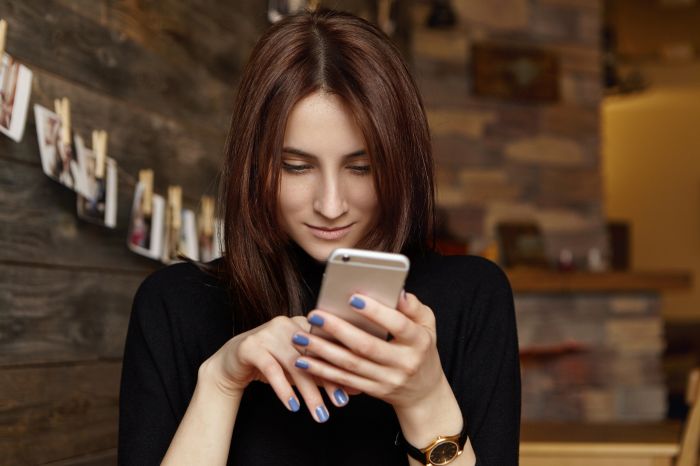 Always in touch. Portrait of charming young brunette European lady browsing newsfeed via social networks, liking posts and typing comments, using free high-speed internet connection at coffee shop