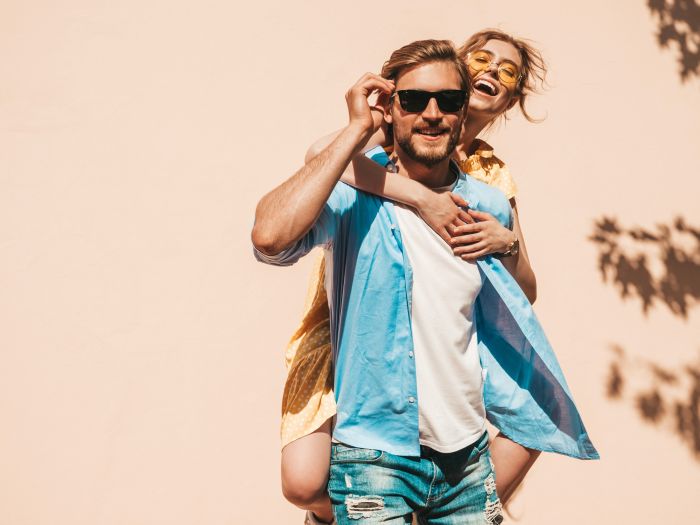 Portrait of smiling beautiful girl and her handsome boyfriend. Woman in casual summer dress and man in jeans. Happy cheerful family. Female having fun in the street near wall