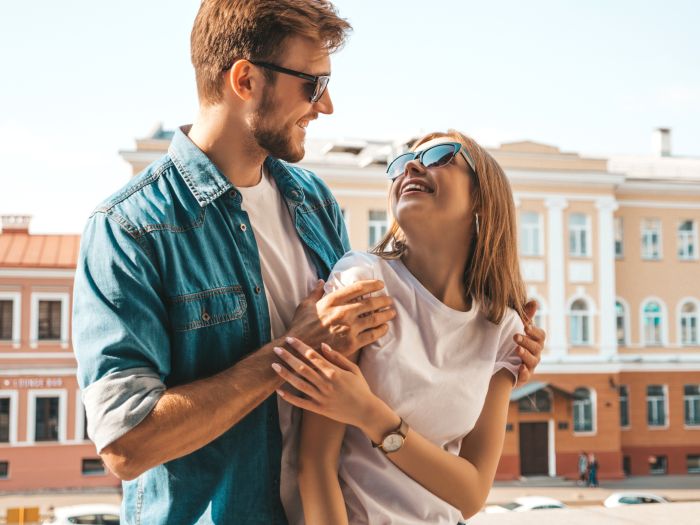 Smiling beautiful girl and her handsome boyfriend. Woman in casual summer jeans clothes. Happy cheerful family. Female having fun on the street background in sunglasses.Looking at each other
