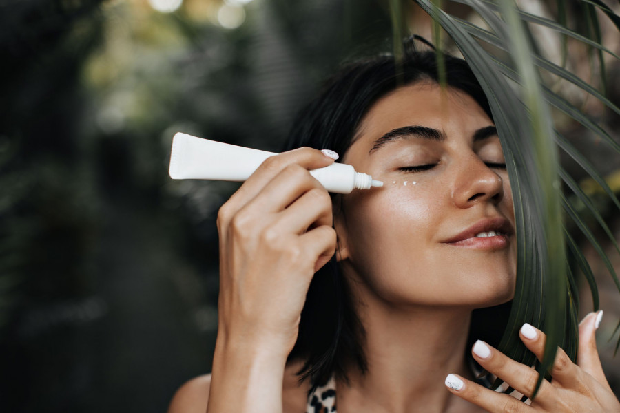 Relaxed woman applying sunscreen. Joyful girl with face cream standing on nature background