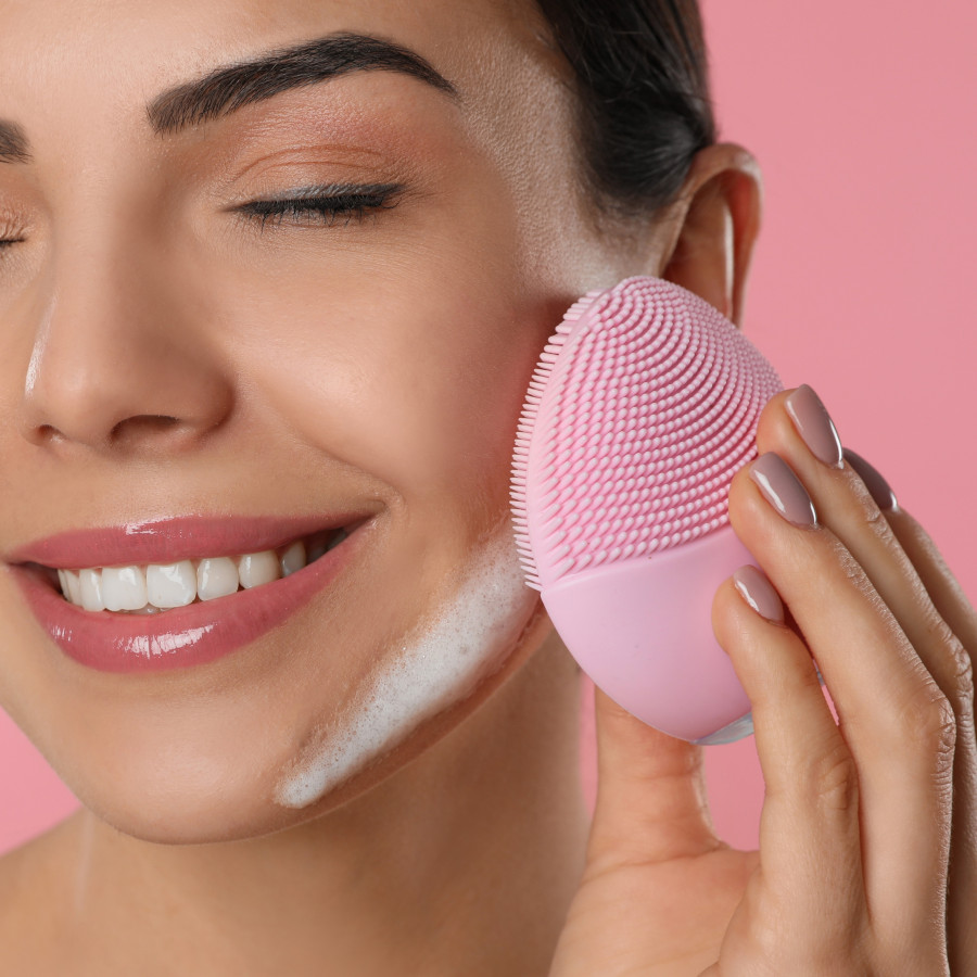 Young,Woman,Using,Facial,Cleansing,Brush,On,Pink,Background,,Closeup.