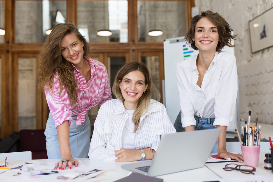 Group of young cheerful women with laptop happily looking in cam