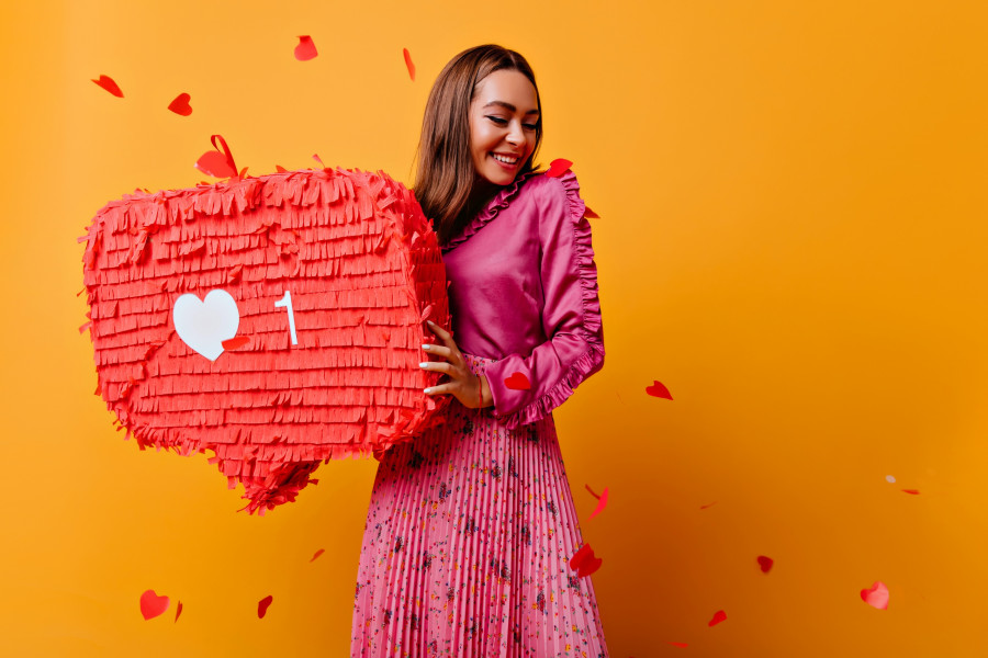 Cheerful girl with pretty smile posing with red bunner. Studio shot of refined brunette female blogger in good mood.