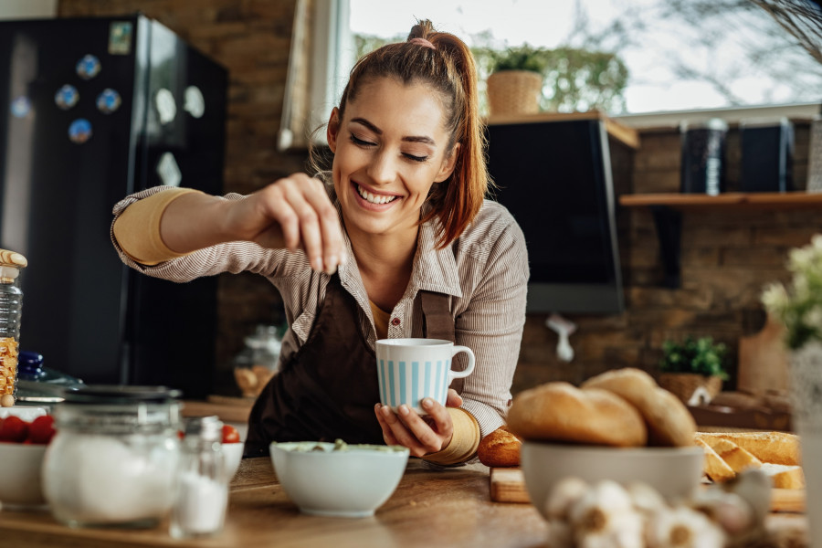 Happy woman seasoning food while cooking in the kitchen.