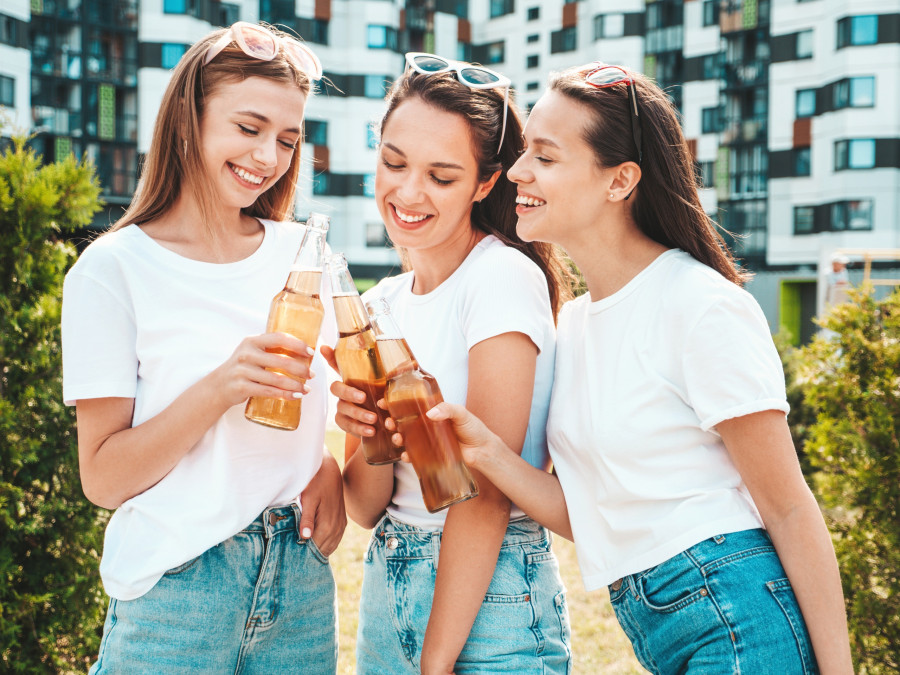 Three young beautiful smiling hipster female in trendy summer same clothes.Sexy carefree women posing in the street.Positive models having fun in sunglasses. Drinking bottle beer. Oktoberfest