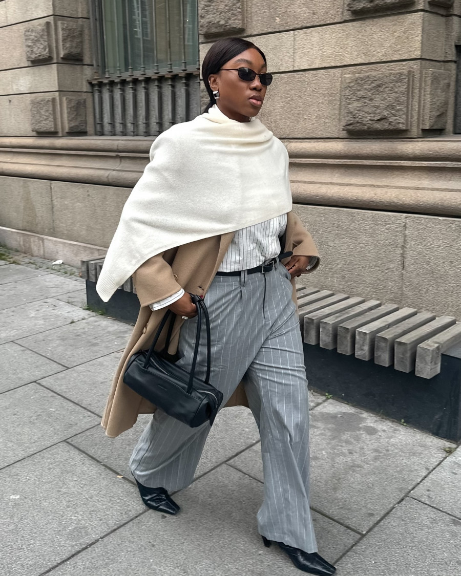 A-chic-city-inspired-outfit-featuring-a-tailored-beige-coat-layered-over-a-striped-shirt-paired-with-gray-pinstripe-wide-leg-trousers.-The-look-is-completed-with-pointed-black-heels-a-sleek-black-handbag.jpg