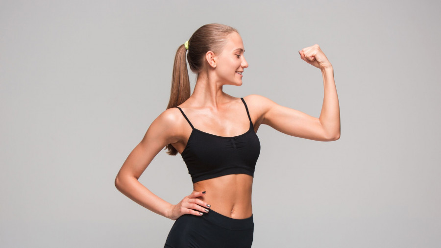 Muscular young woman athlete on gray