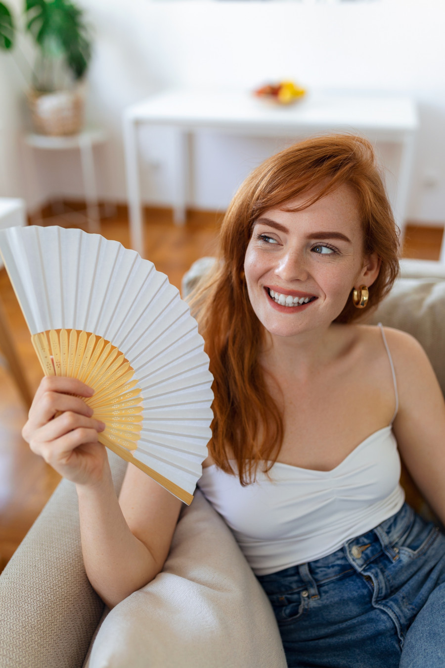 Close up overheated woman waving paper fan, breathing air, leaning back on couch alone, suffering from heating, fever or hot summer weather at home