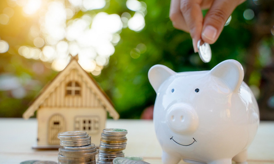 Saving money concept to buy a house by Piggy bank with coin stack and toy house.