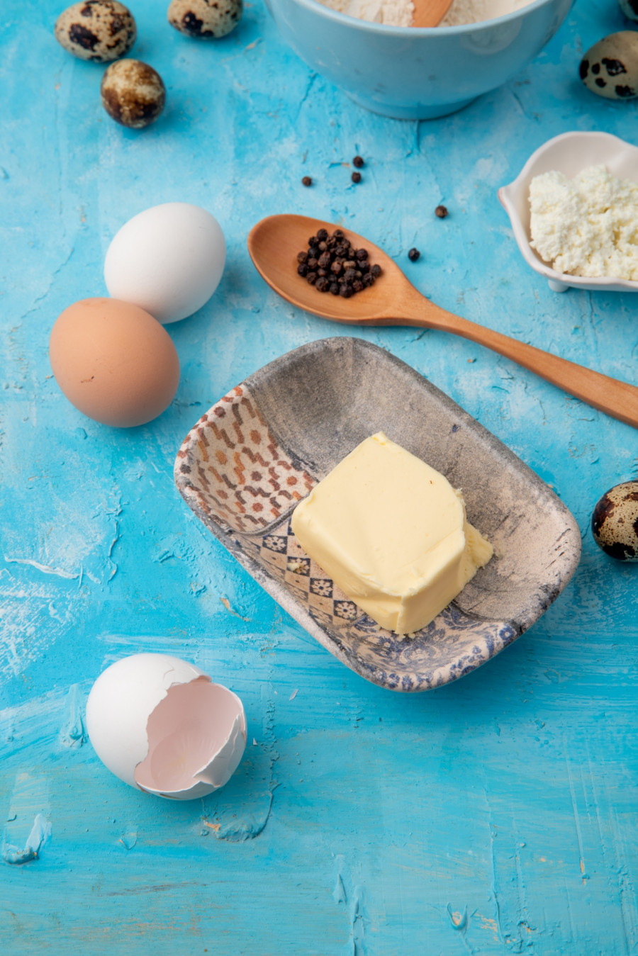 side view of plate of butter and eggshell with eggs on blue background