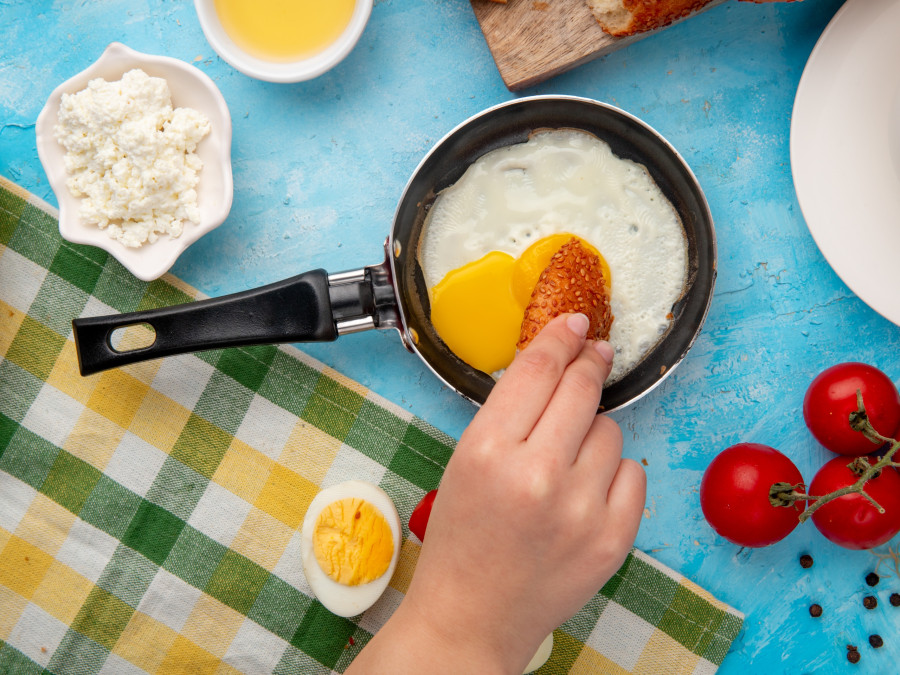 close-up view of woman hand eating fried egg with cottage cheese tomato black pepper on blue background