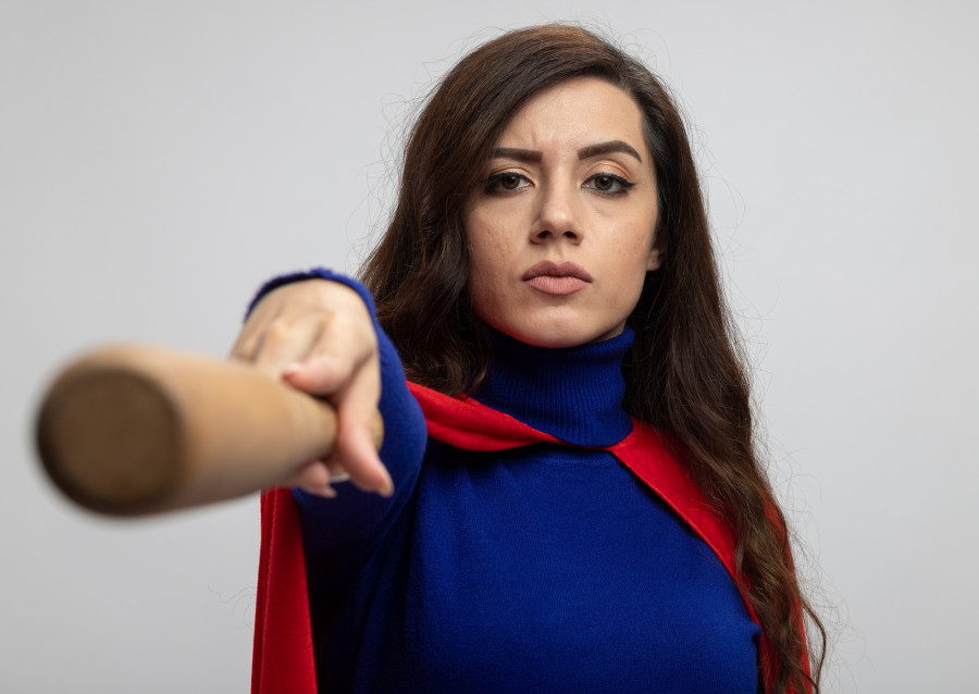 confident caucasian superhero girl with red cape holds out baseball bat isolated on white background with copy space
