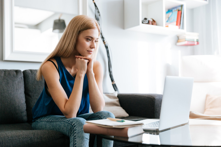 Concentrated young woman sitting and working with laptop at home