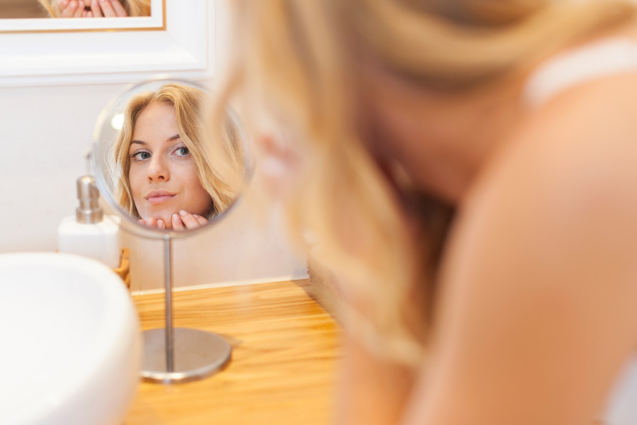 Woman caring about her skin on face in front of small mirror