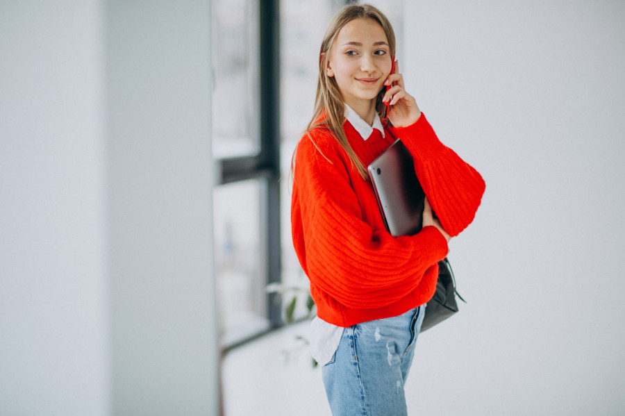 Girl student holding computer and talking on the phone by the window