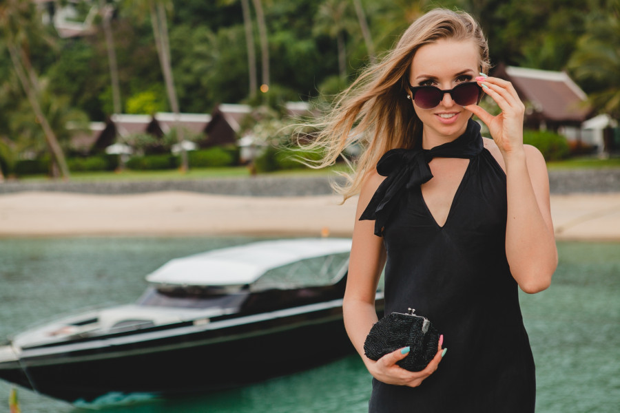 luxury sexy attractive woman dressed in romantic black dress posing on pier in luxury resort hotel, wearing sunglasses, summer vacation, tropical beach