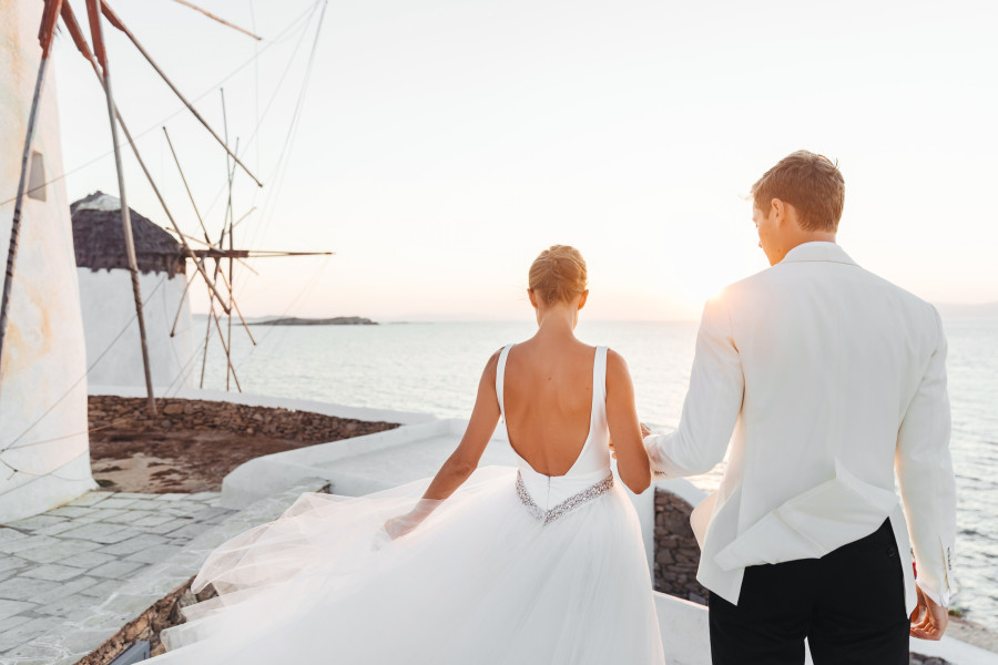 Bride and groom walk towards the sunset over the sea