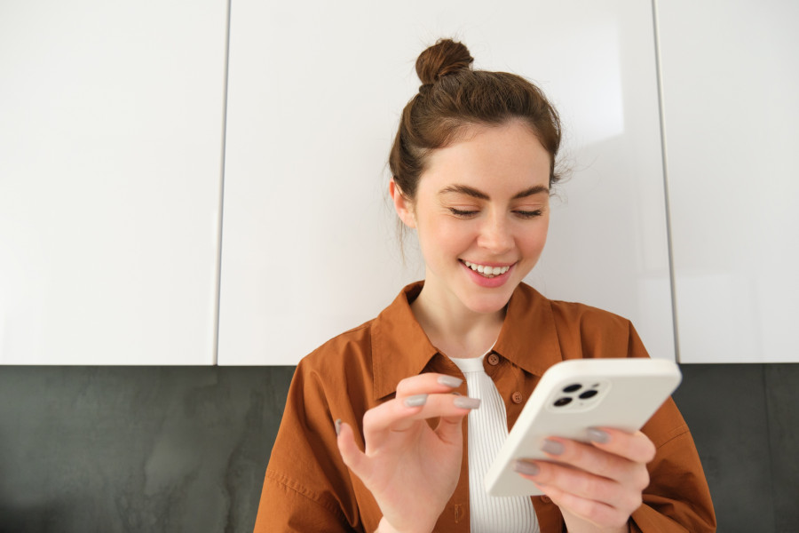 Happy girl with smartphone, looking at phone and smiling, standing at home, concept of buying online, shopping in mobile app